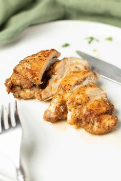 a white plate topped with chicken next to a knife and fork