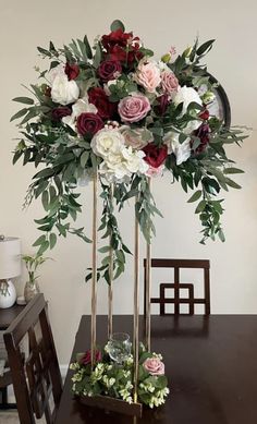 a vase with flowers and greenery on top of a table next to a chair