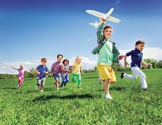 a group of children running in the grass with a toy airplane