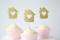 three cupcakes with gold glitter toppers on white frosting and pink icing