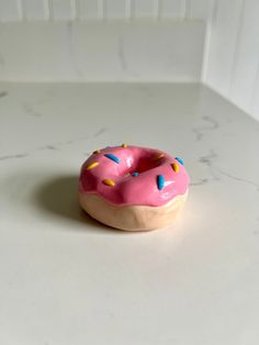 a pink doughnut with sprinkles sitting on top of a white counter