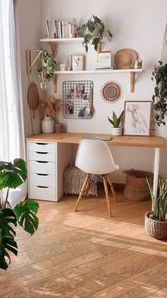 a room with some plants and pictures on the wall, including a desk in front of a window