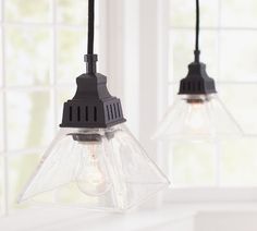 two clear glass pendant lights hanging from a ceiling fixture in a room with white walls and windows