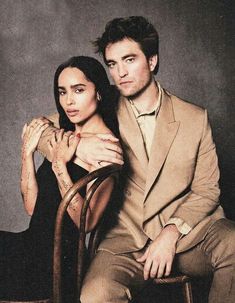 a man and woman sitting next to each other on a wooden chair in front of a gray background