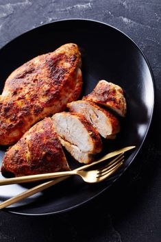 two pieces of chicken on a black plate with gold forks