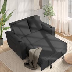 a black couch sitting on top of a wooden floor next to a potted plant