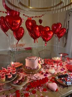 a table topped with lots of heart shaped balloons and cupcakes on top of it