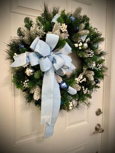 a christmas wreath with blue and white decorations hanging on the front door to welcome guests