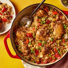 a pan filled with rice and vegetables on top of a yellow tablecloth next to two plates of food