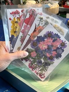 a person is holding some flowers in their hand and there are other pictures on the table