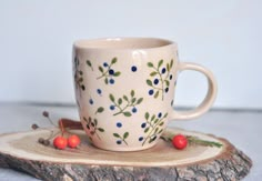 a coffee cup sitting on top of a piece of wood next to some red berries