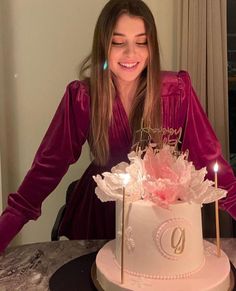 a woman in a purple dress is cutting into a white cake with candles on it