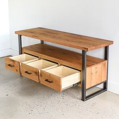 a wooden table with drawers underneath it on concrete floor next to white wall and black metal frame