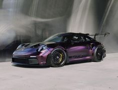 a purple and black sports car parked in front of a wall with water flowing down it