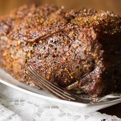 a piece of meat on a white plate with a fork and lace doily next to it