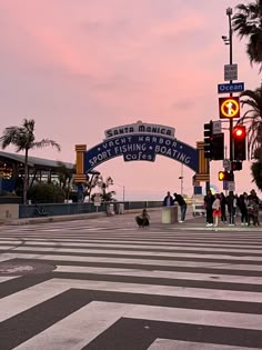 people are crossing the street in front of some palm trees and buildings at sunset or dawn