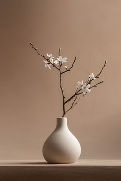 a white vase filled with flowers on top of a wooden table next to a wall