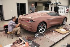 two men working on a car that is being made out of wood and plastic in a garage