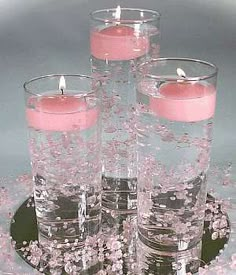 four candles are placed in glass vases with water and pink flowers on the table