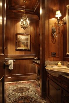 a fancy bathroom with wood paneling and chandelier above the sink, along with a rug on the floor