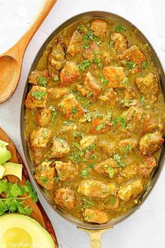 a pan filled with meat and vegetables next to an avocado on the side