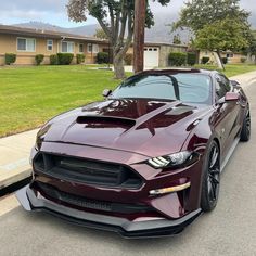 a maroon mustang is parked on the side of the road in front of some houses