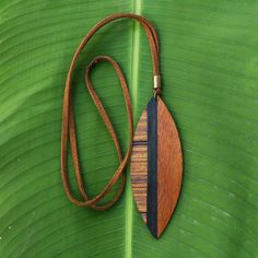 a wooden necklace hanging on a green leaf with a brown leather cord attached to it