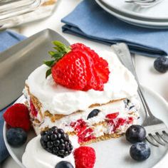 a piece of cake on a plate with berries and whipped cream around the edges, next to a knife and fork