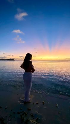 a woman standing on top of a sandy beach next to the ocean at sunset or dawn