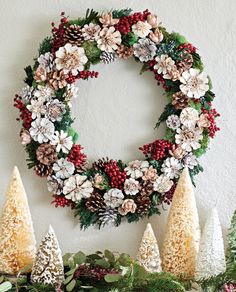 a christmas wreath is hanging on the wall next to pine cones and evergreens with berries