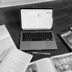 an open laptop computer sitting on top of a wooden table next to books and papers