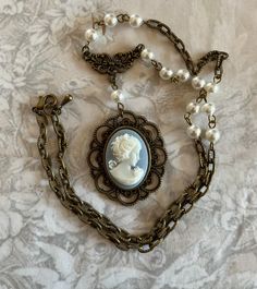 Hand crafted necklace vintage resin cameo of Victorian lady. The cameo is from the 1960s. White on Wedgwood blue background. It's set in an antiqued style brass bezel.  Vintage faux Japan pearls and brass chain. It's 18 inches end to end and adjustable. So it can be worn snug as a choker or loser. It has an Art Deco brass connector.  Comes gift boxed. Cameo Choker Necklace, Wedgwood Blue, Victorian Lady, Cameo Jewelry, Cameo Necklace, Handcrafted Necklace, Brass Chain, Antique Style, Blue Fashion