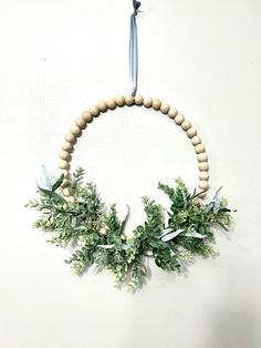 a wooden beaded wreath with greenery hanging from the side on a white wall