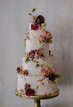 a three tiered cake with flowers and leaves on the top is sitting on a gold pedestal