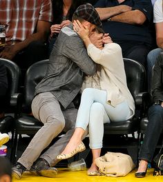 a man and woman sitting next to each other in front of a crowd at a basketball game