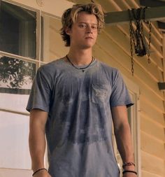 a young man standing in front of a house wearing a blue shirt and bracelets