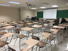 an empty classroom with desks and chairs in front of a projector screen on the wall