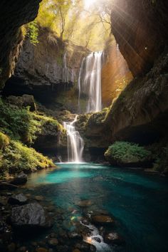 a waterfall in the middle of a forest with blue water and green trees around it