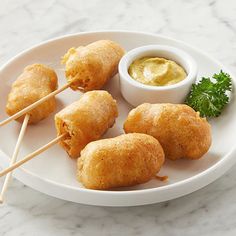 some food is on a white plate with toothpicks and dipping sauce in the bowl