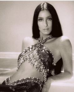 a black and white photo of a woman in a belly dance outfit sitting on a ledge