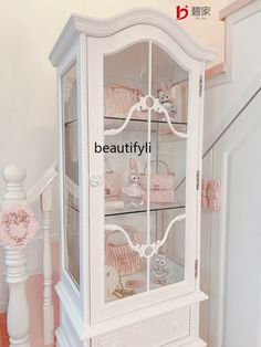 a white china cabinet sitting on top of a wooden floor next to a stair case