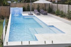 an empty swimming pool with lounge chairs and umbrellas in the back yard, next to a wooden fence