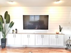 a large flat screen tv mounted on the wall in a living room with white cabinets