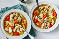 two bowls of chicken and vegetable soup on a white table with a blue napkin next to it