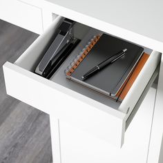 a desk with a pen, notebook and phone in it on top of a drawer