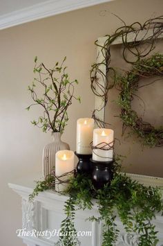 candles are sitting on top of a mantle with greenery and branches in front of it