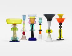 there are many different colored glass vases on the table together, including one with a yellow shade