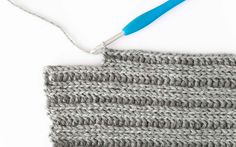 the crochet pattern is being worked on with a blue handled knitting needle and yarn