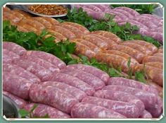 many sausages are stacked on top of each other in front of green plants and food