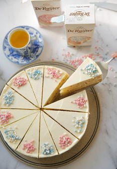 a cake with white frosting and sprinkles on it next to a cup of tea